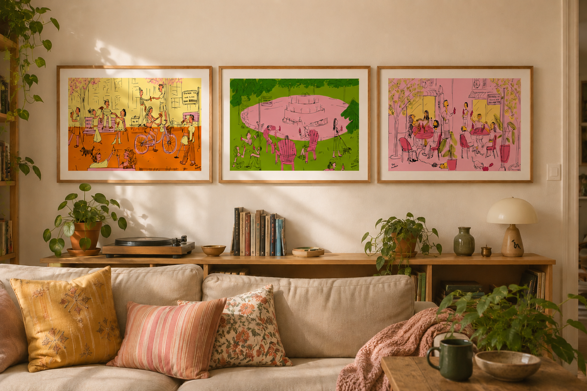 Three framed art prints with colorful retro-style illustrations hang on a beige wall above a wooden console shelf in a cozy living room setting with plants, pillows, and a lamp.